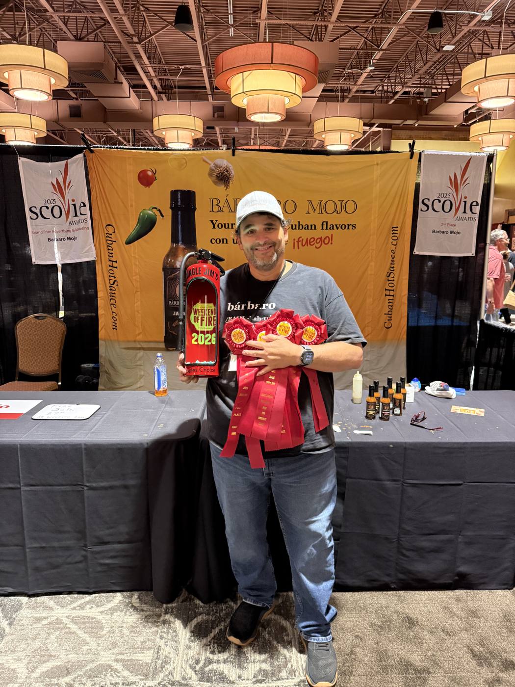 Mario Cruz holding Weekend of Fire 2026 award ribbons and the Peoples Choice trophy at the Barbaro Mojo booth
